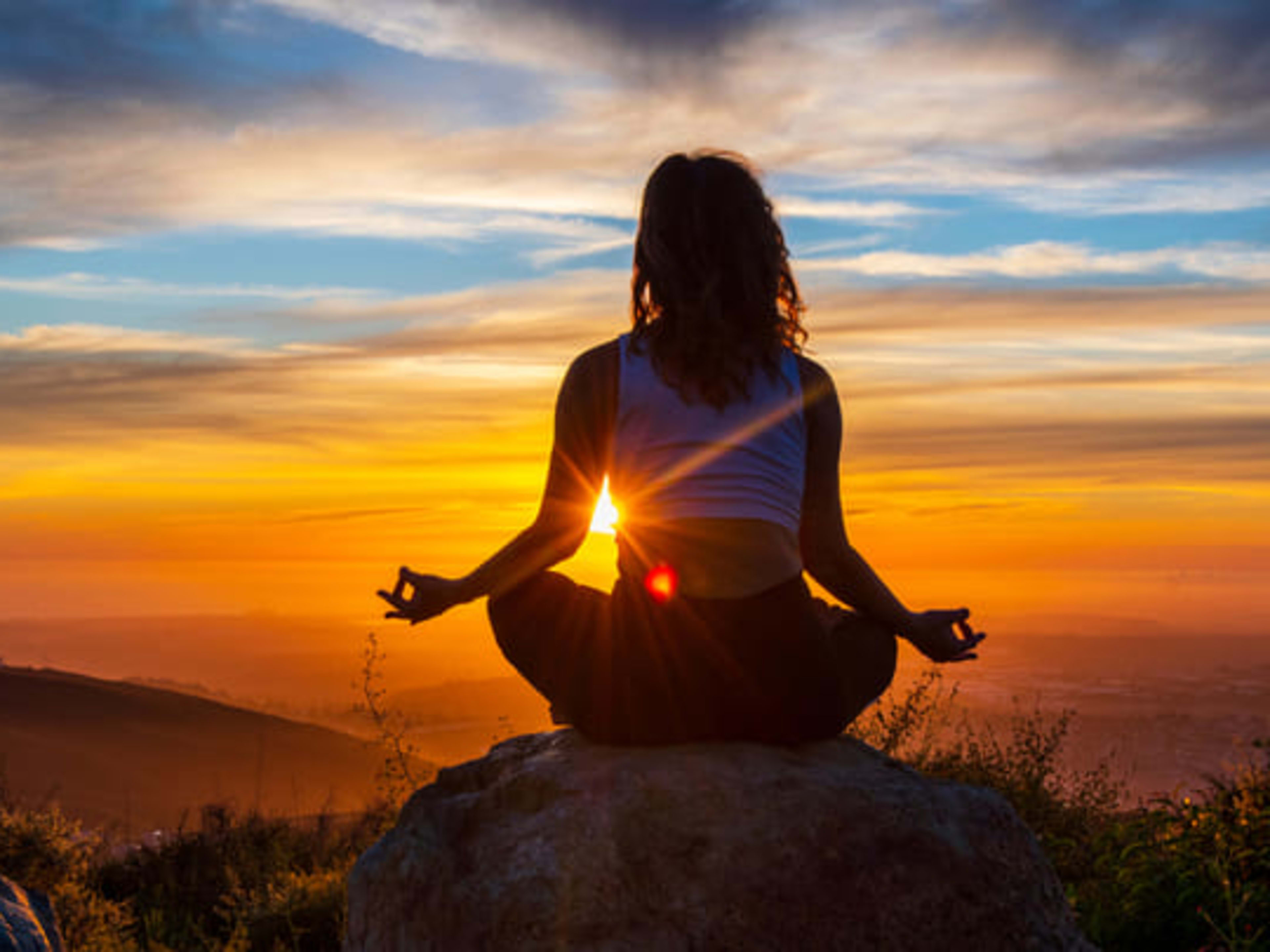 Mulher meditando em uma rocha ao pôr do sol em San Diego