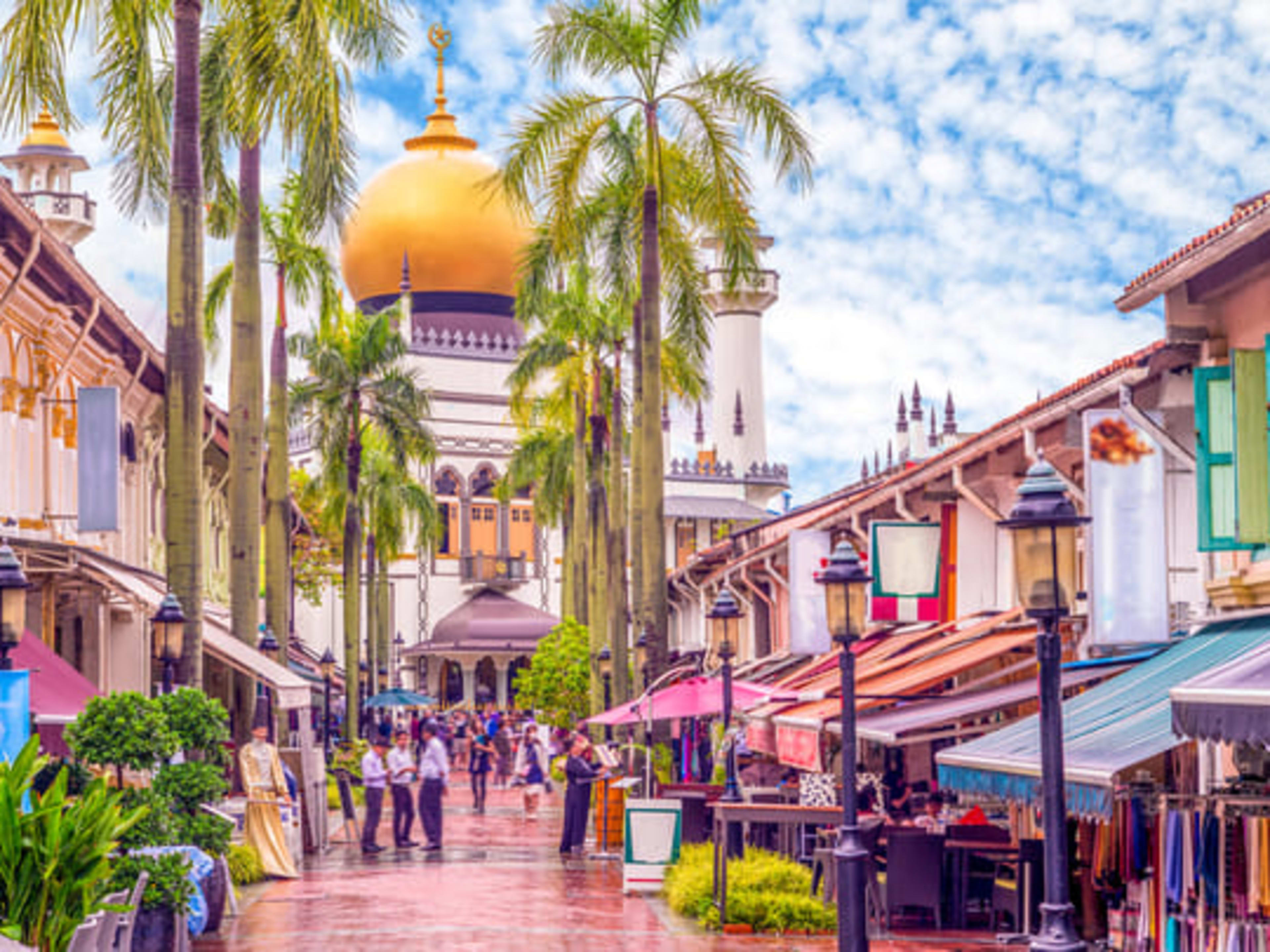 The colorful Kampong Glam district in Singapore, with the golden dome of the Sultan Mosque visible behind the palm trees.