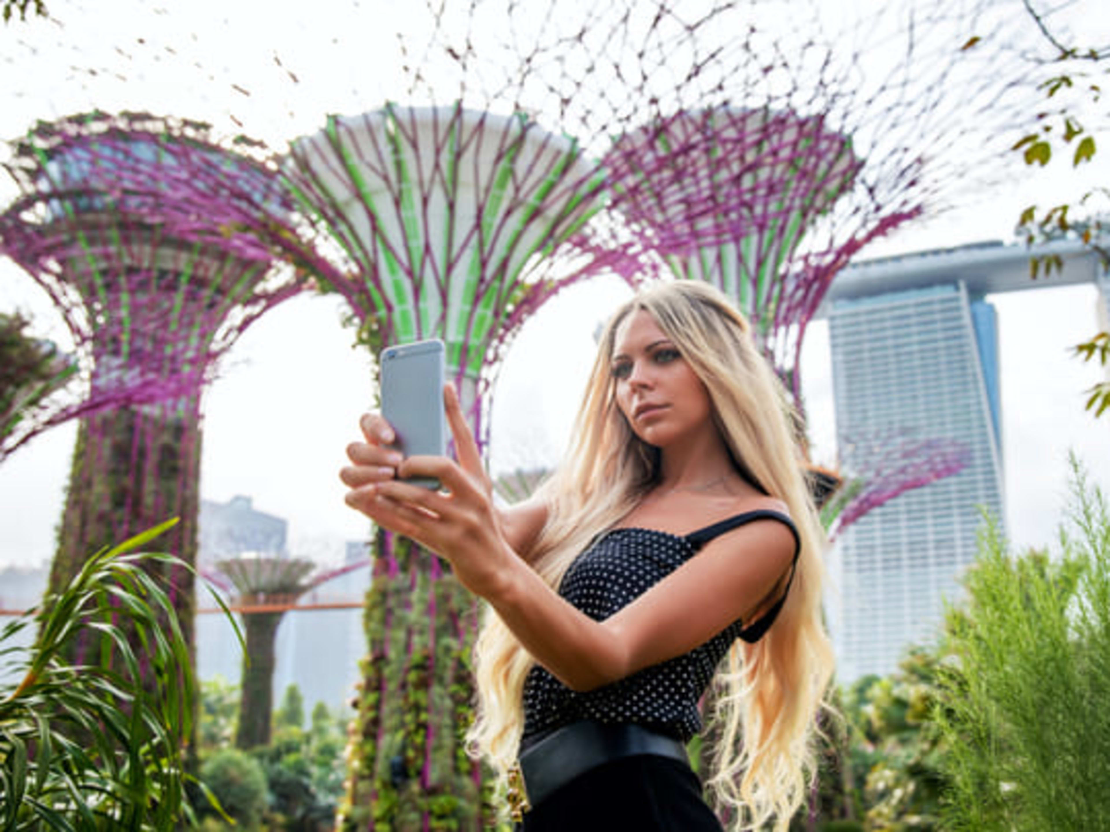 Young woman taking a selfie in front of the supertree structures at the Gardens by the Bay, Singapore