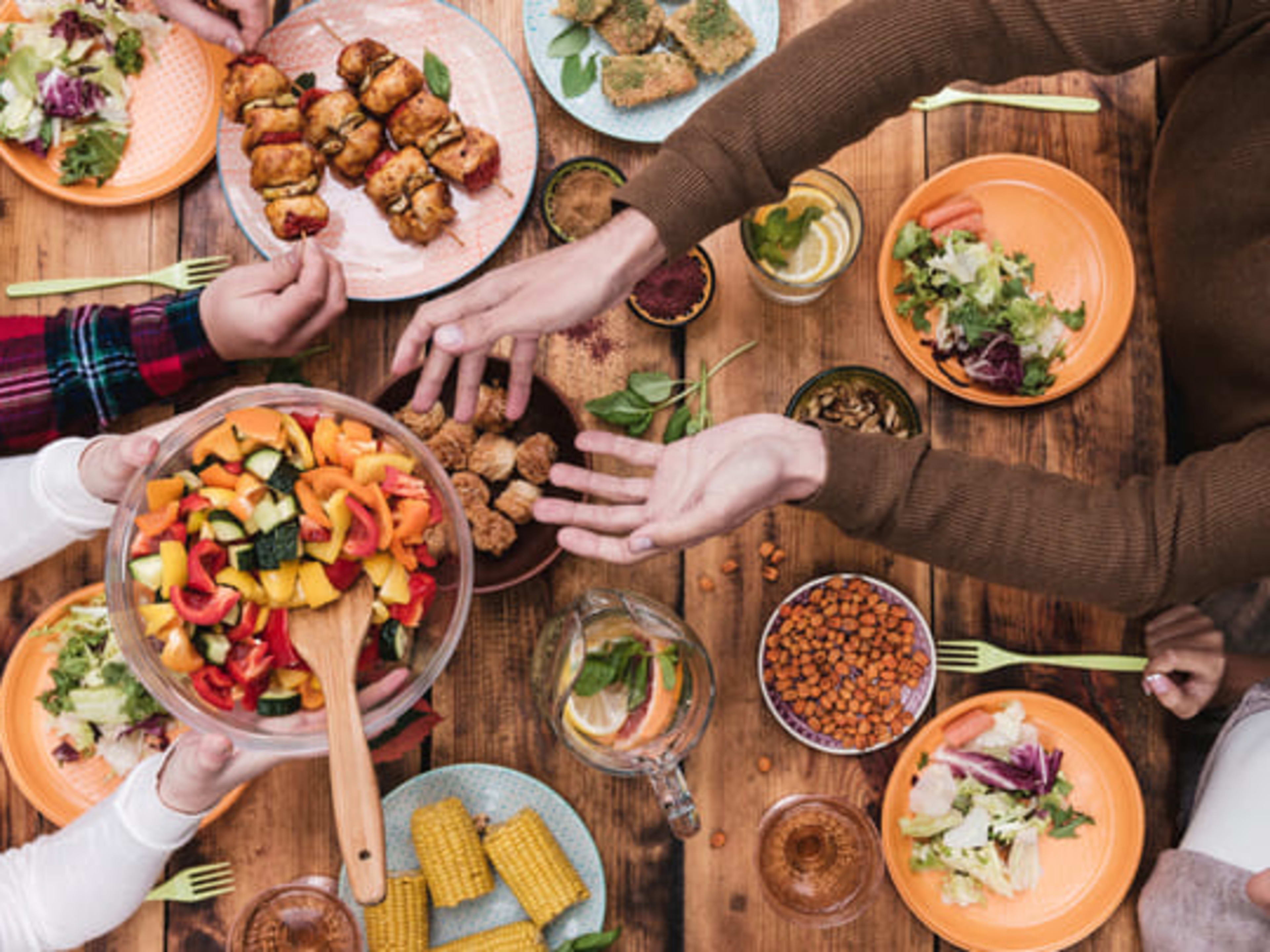 Amigos compartilhando comida vegetariana em uma grande mesa coletiva.