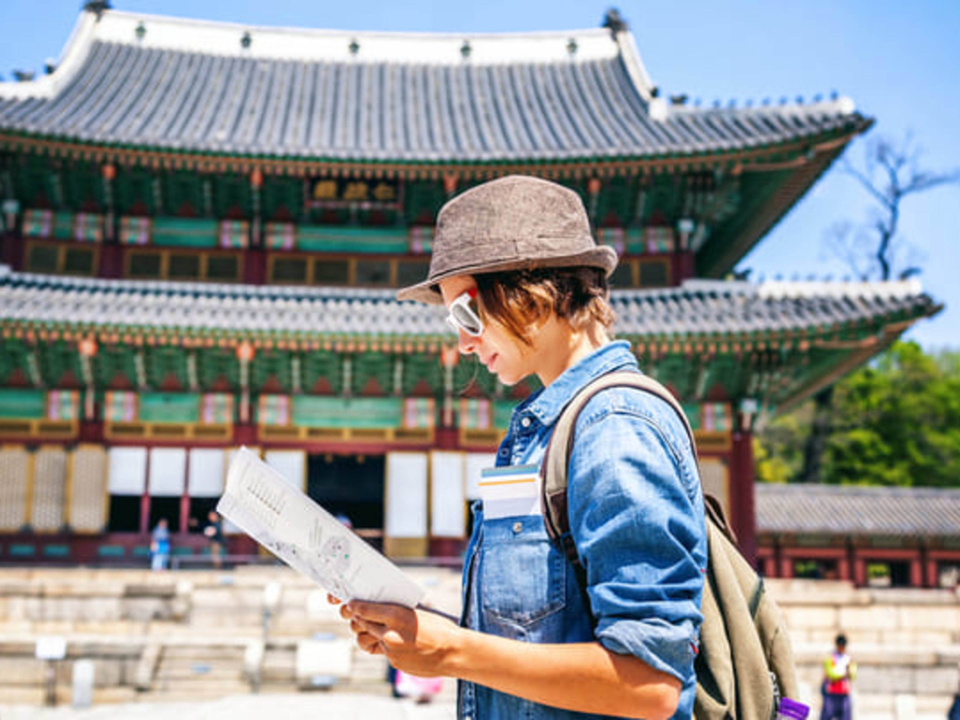 Woman studying a map in front of a pagoda-style building in Seoul.