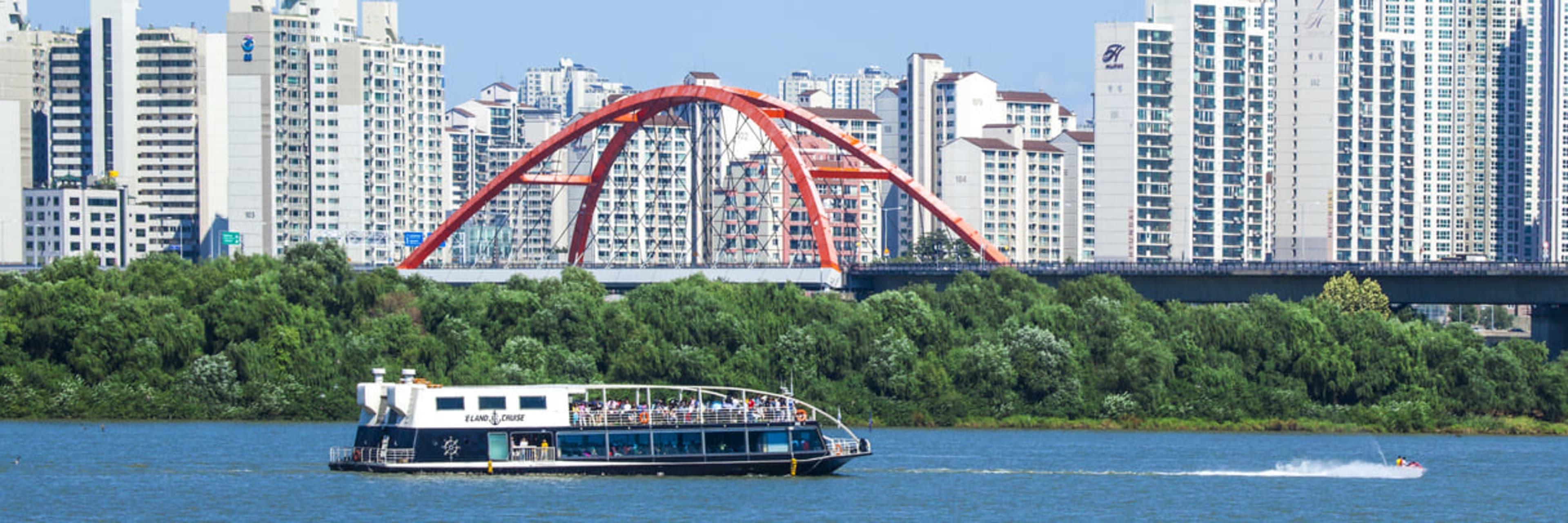 The E-land Han River cruise boat illuminated against Seoul's city skyline at sunset.