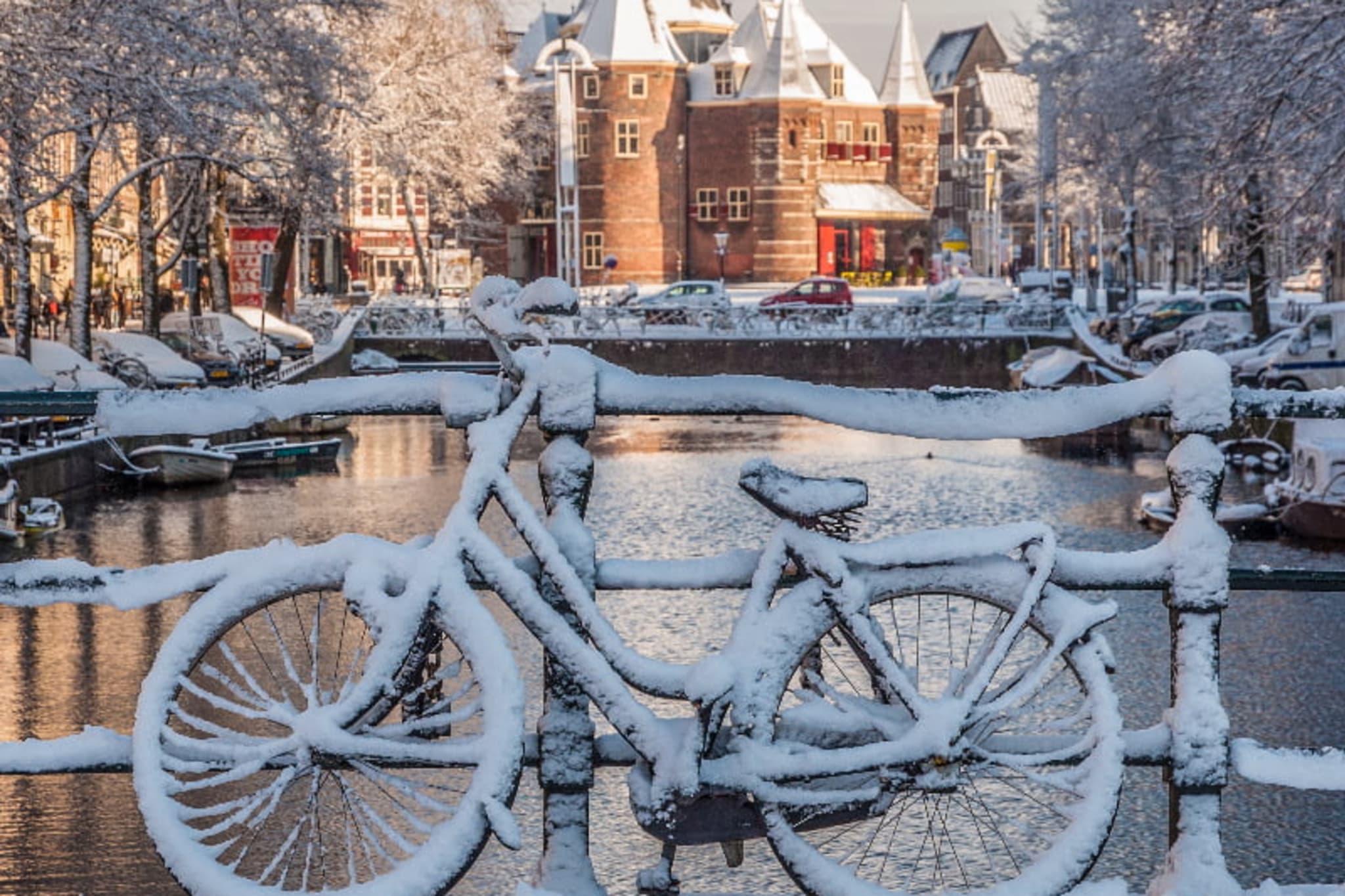 Snowed-covered bicycle leaning against a bridge over an Amsterdam canal