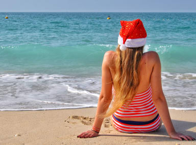 A woman on a beach facing the sea in a Santa hat