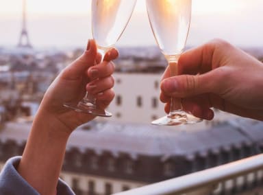 Close up of two hands raising a champagne toast with Paris/Eiffel Tower in background