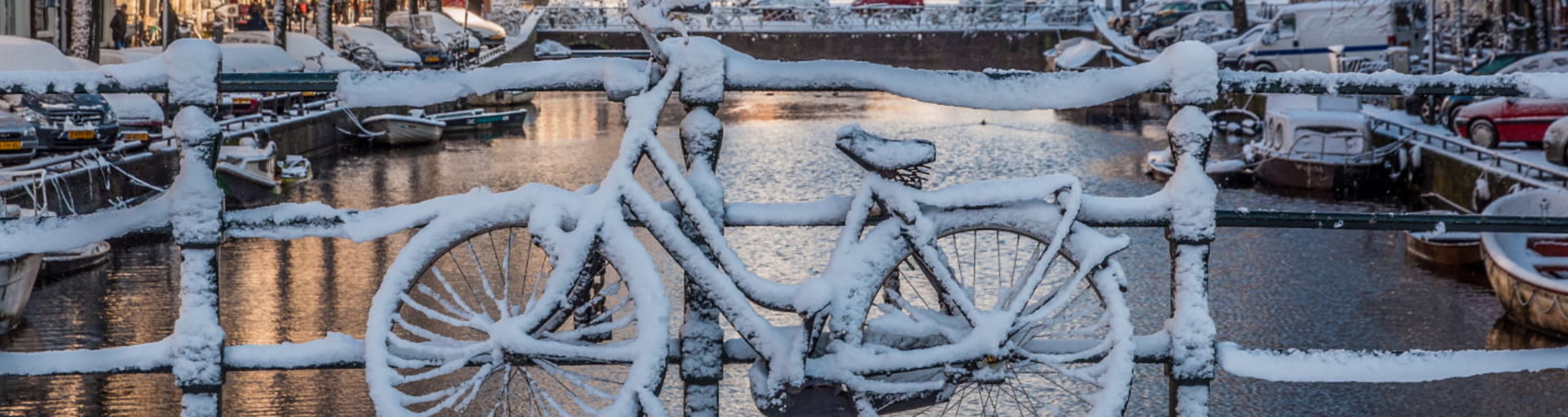 Snowed-covered bicycle leaning against a bridge over an Amsterdam canal