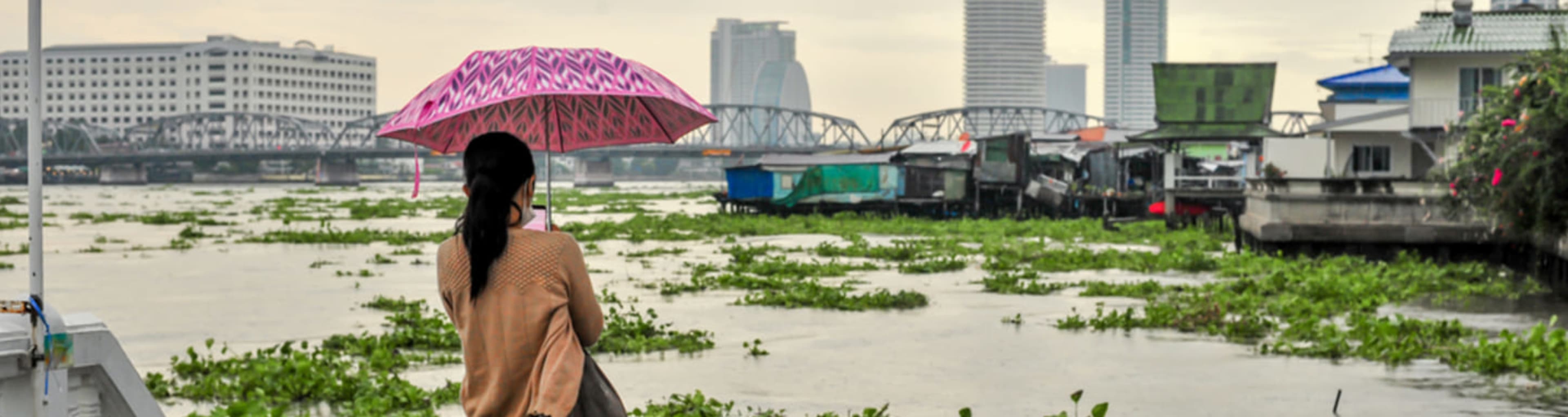 Woman gazing across the Chao Phraya river at the Bangkok skyline during a monsoon.