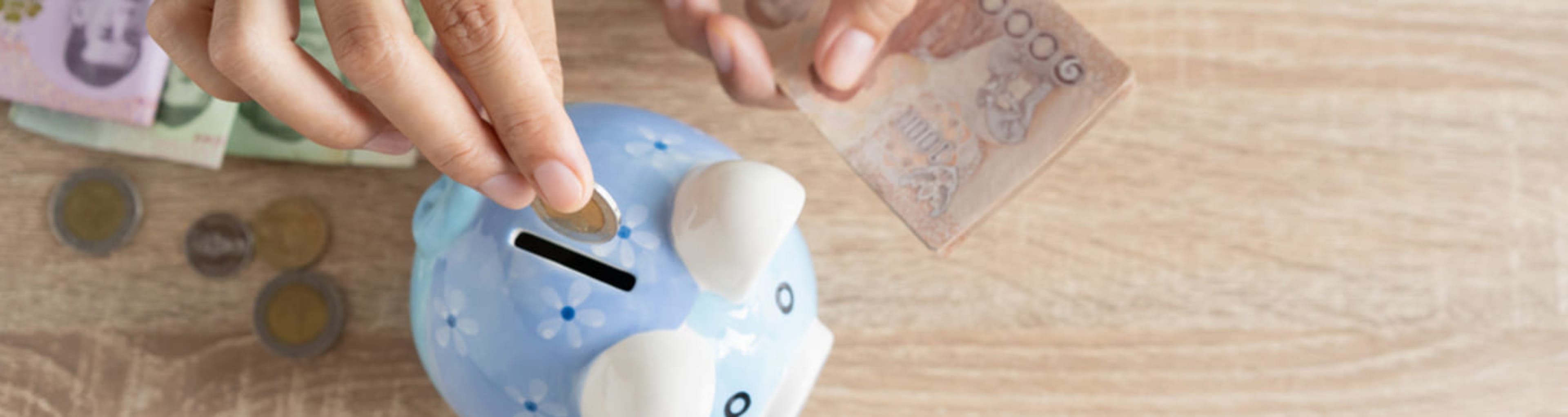 Pair of hands placing coins and notes in a piggy bank.