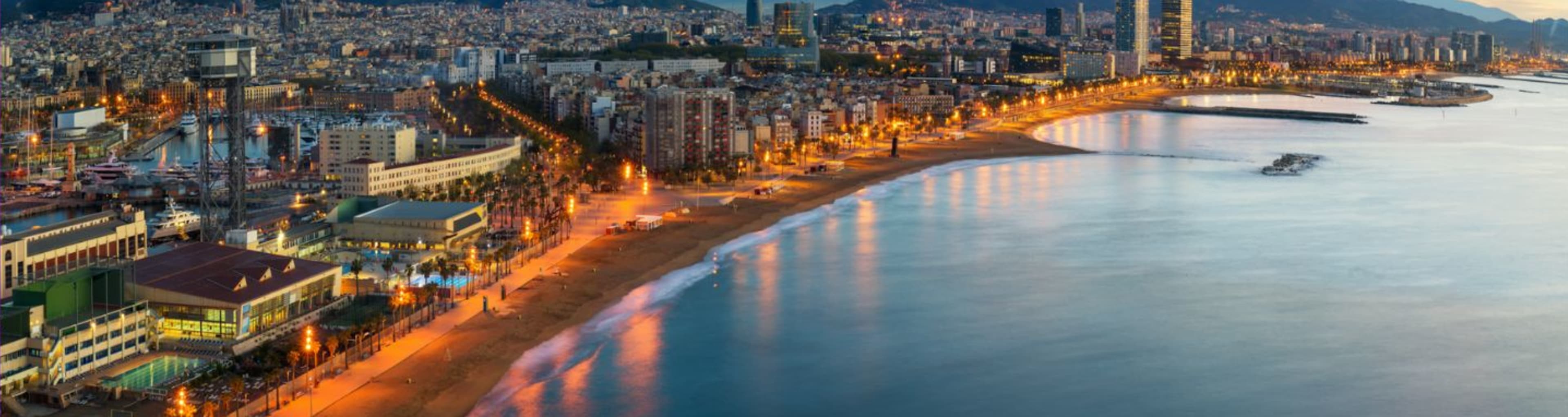 Wide view of Barcelona showing the curve of the bay and the lights of the city as golden evening falls