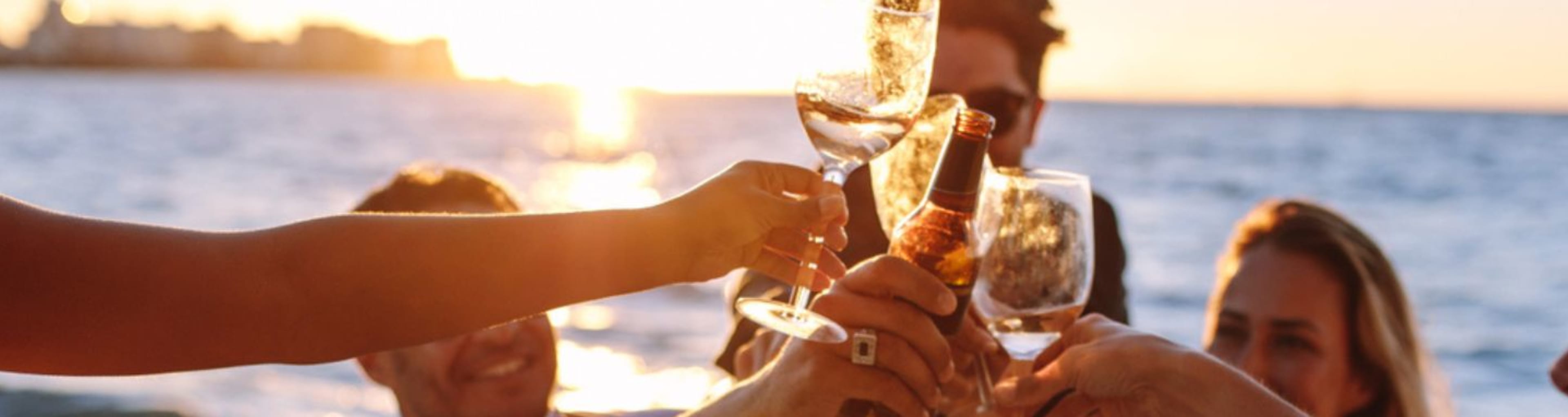 Close up of adult hands raising a toast with wine glasses against sunset sea