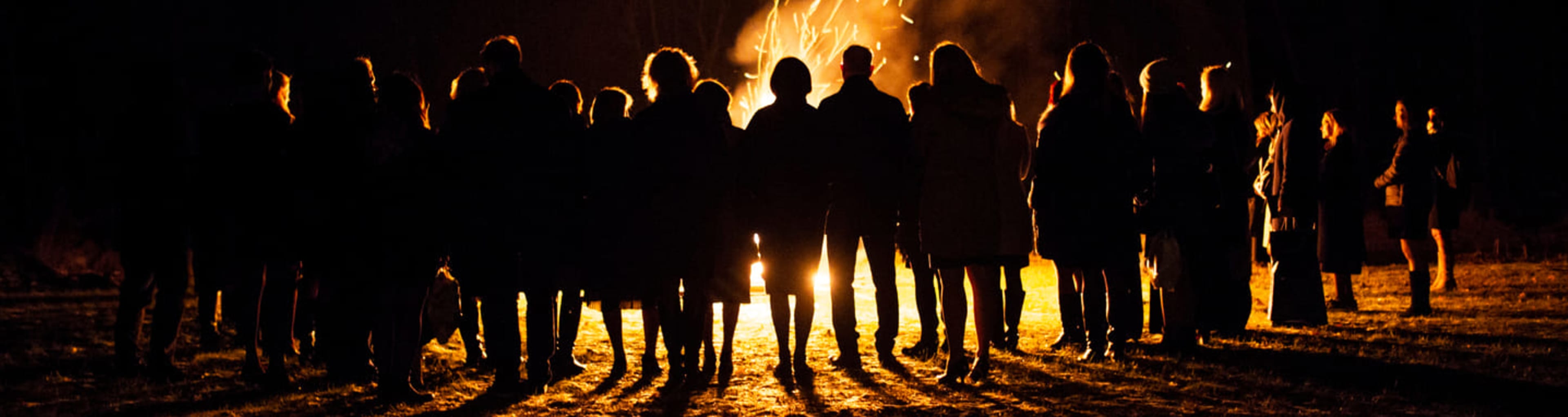 Group of people silhouetted against a beach bonfire at night