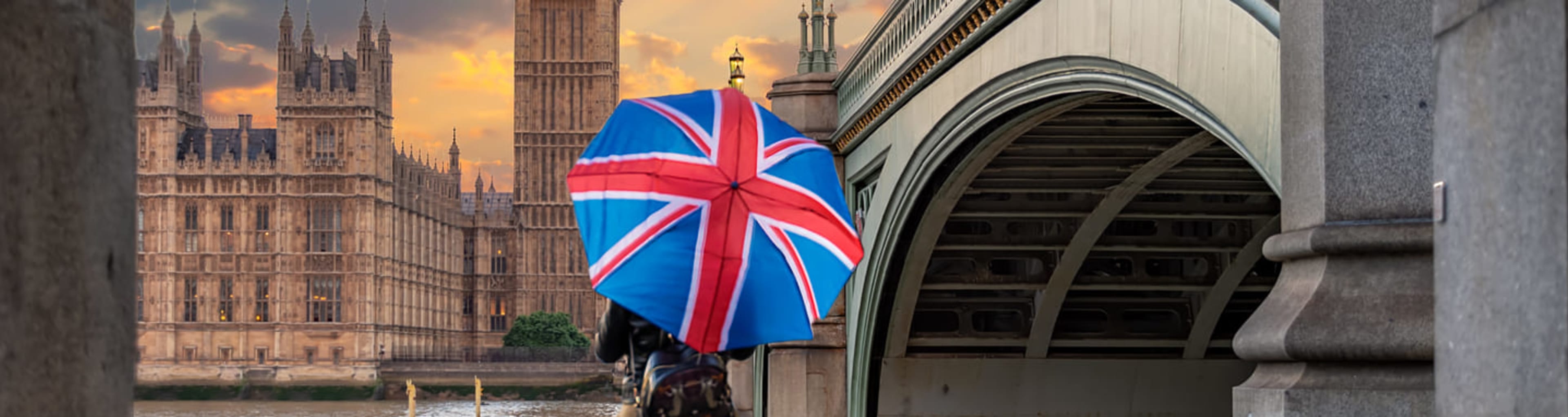 Tourist with Union Jack umbrella looking at Big Ben across the River Thames