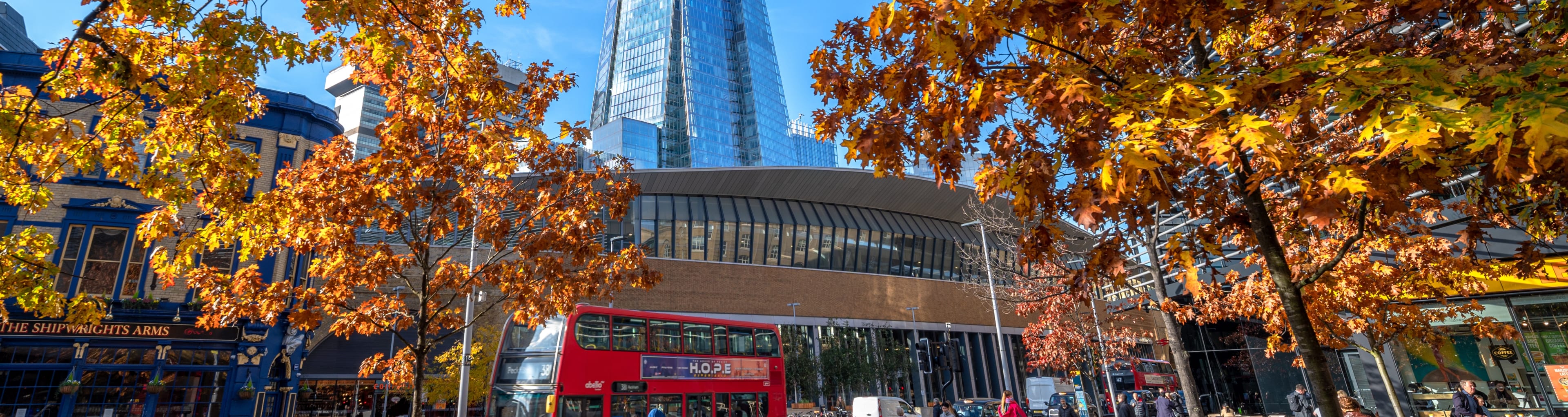 Herbstszene mit orangefarbenen Bäumen vor dem Londoner Bahnhof und dem berühmten Wahrzeichen Shard an einem sonnigen Tag.