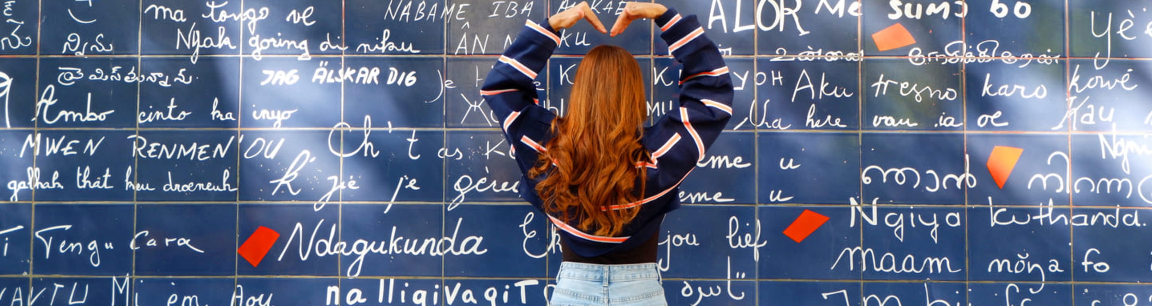 Woman making a heart shape with her arms in front of Montmartre's Wall of Love