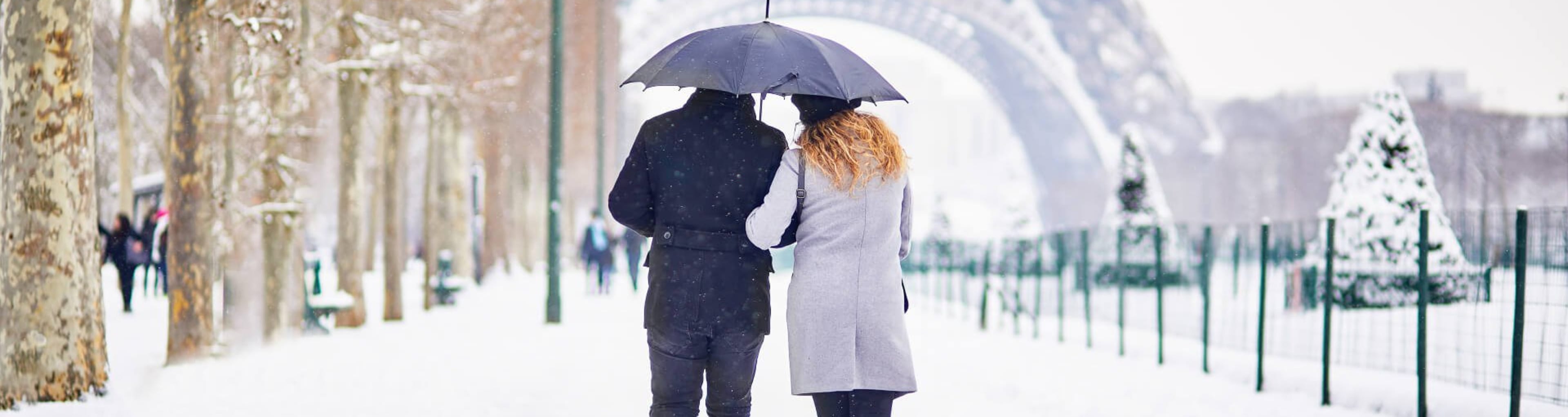 A couple walk in the snow towards the Eiffel Tower