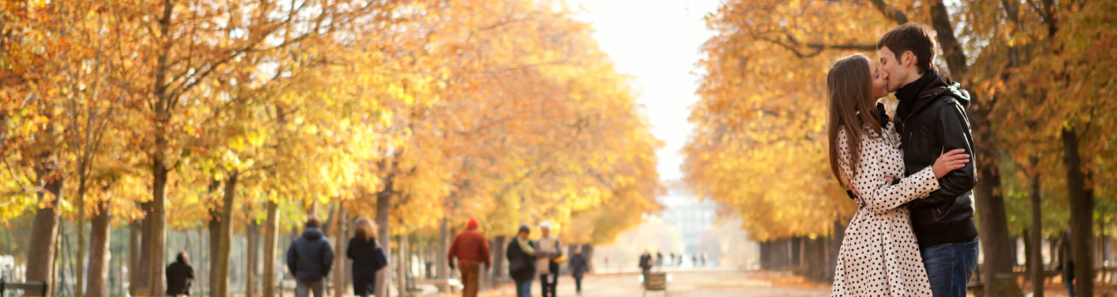 A couple share a kiss beneath the falling leaves of the Jardin de Luxembourg