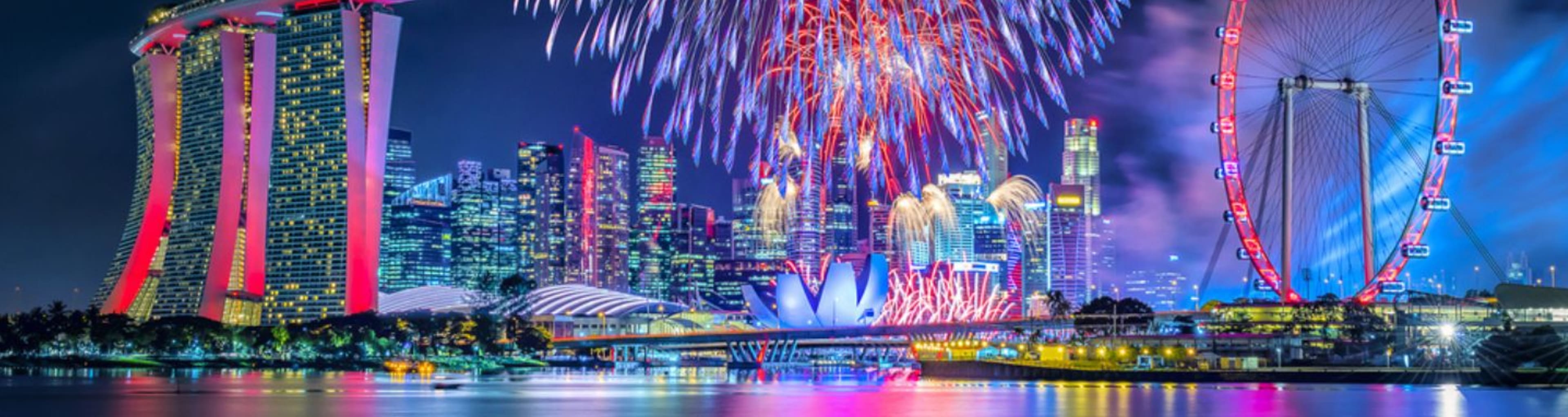 The lights of the Singapore skyline reflected in water as multicoloured fireworks explode above