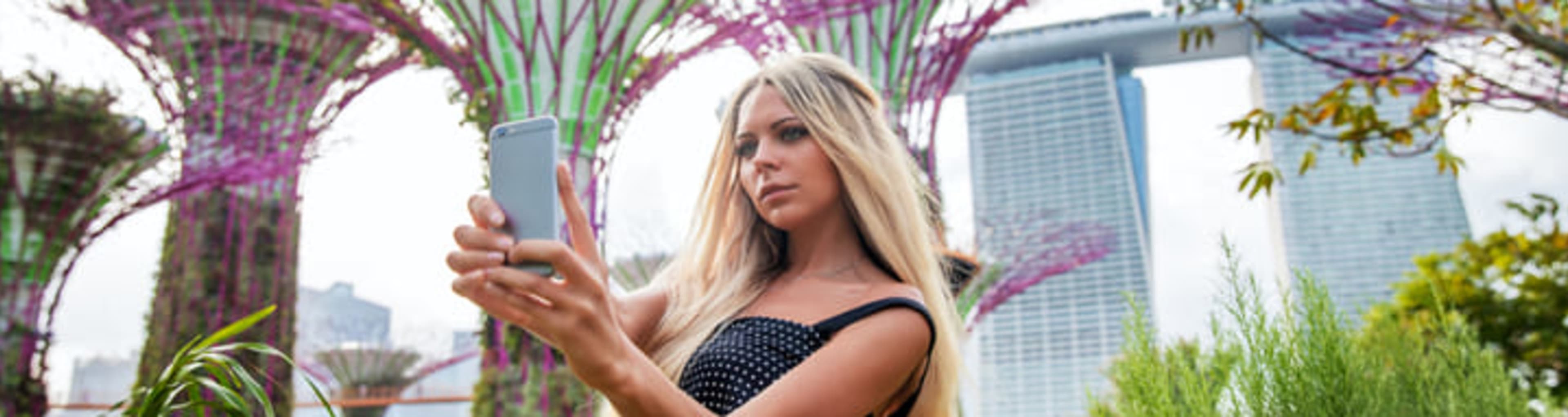 Young woman taking a selfie in front of the supertree structures at the Gardens by the Bay, Singapore