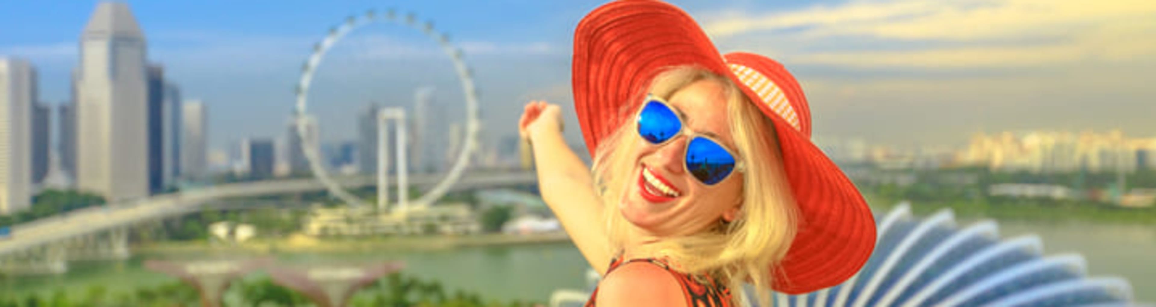 Woman in a red hat smiling and pointing towards the distant Singapore Flyer