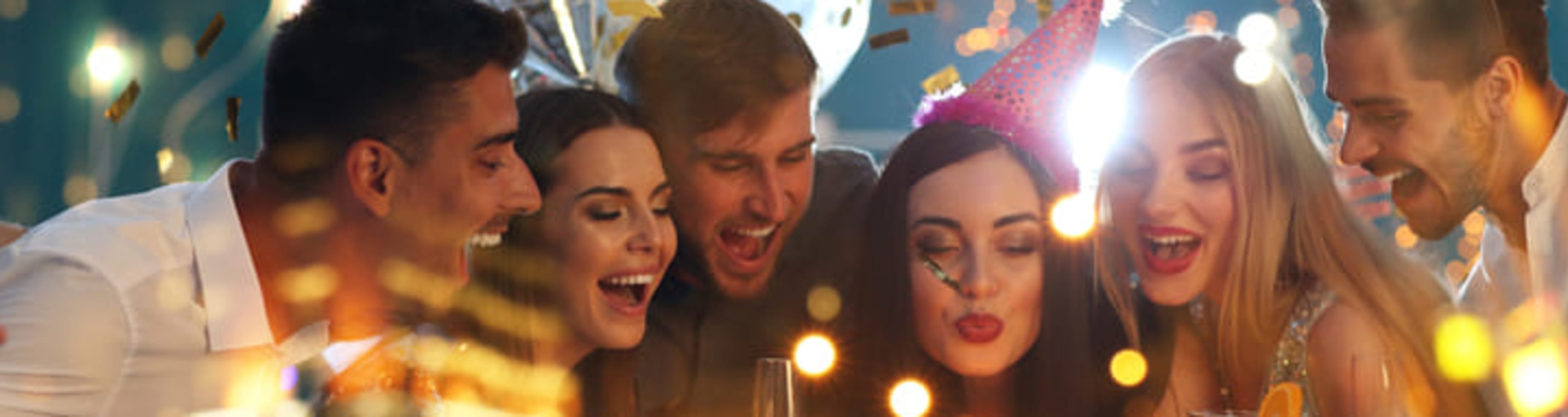 Group of friends celebrating a birthday by blowing out candles on a cake