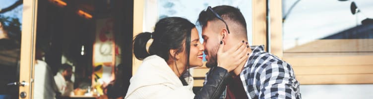 A couple lean in for a kiss at a cafe table