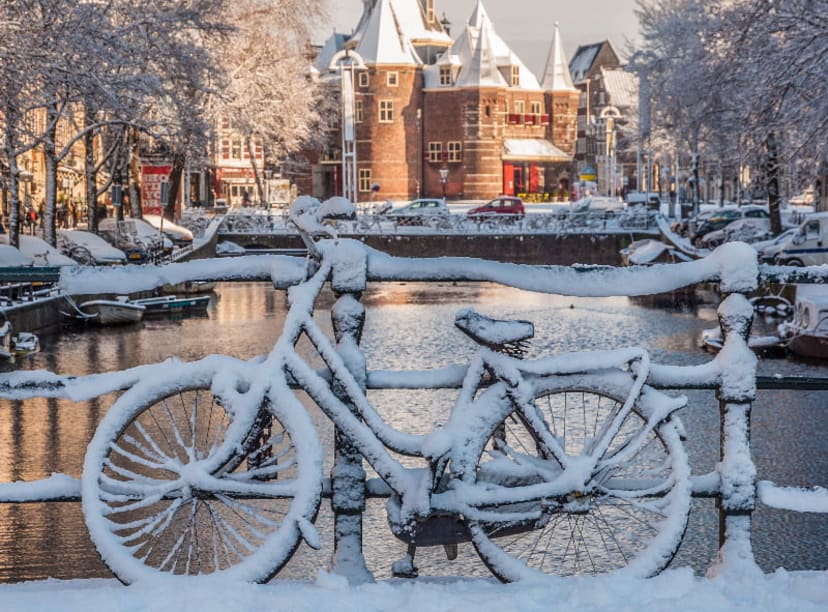 Snowed-covered bicycle leaning against a bridge over an Amsterdam canal