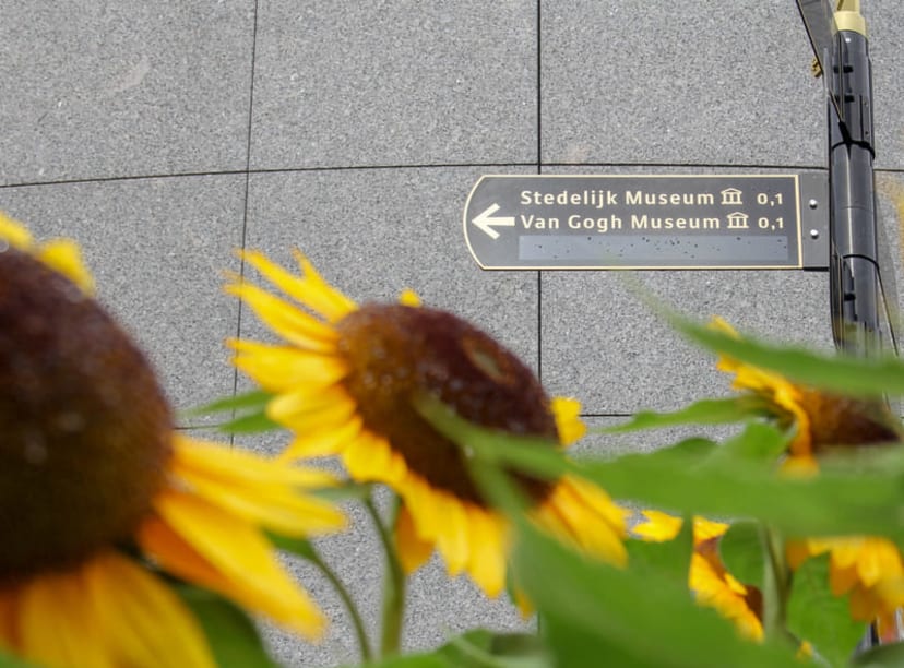 Sunflowers in front of a street sign pointing towards the Van Gogh Museum.