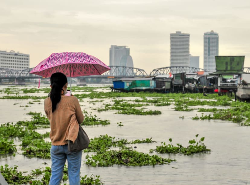 Woman gazing across the Chao Phraya river at the Bangkok skyline during a monsoon.