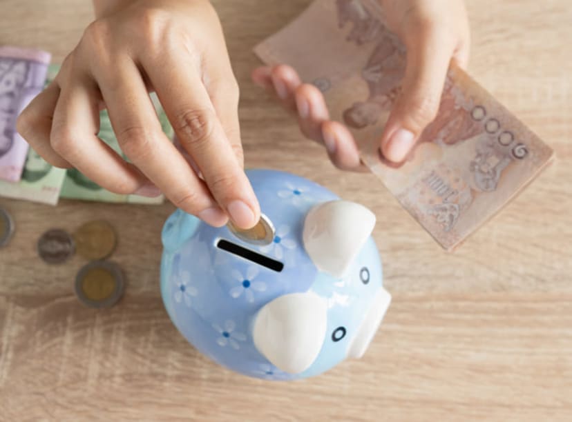 Pair of hands placing coins and notes in a piggy bank.