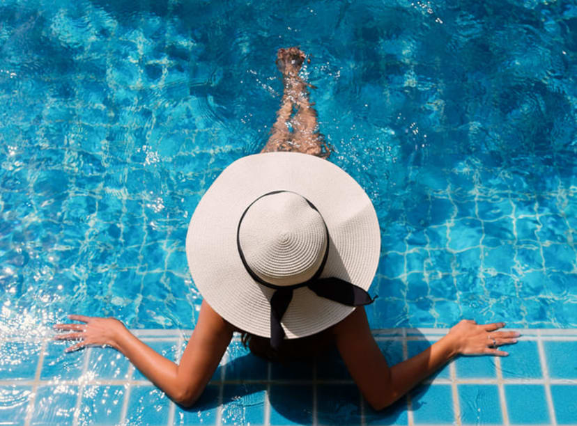 Aerial view of woman wearing a large sun hat in a swimming pool.