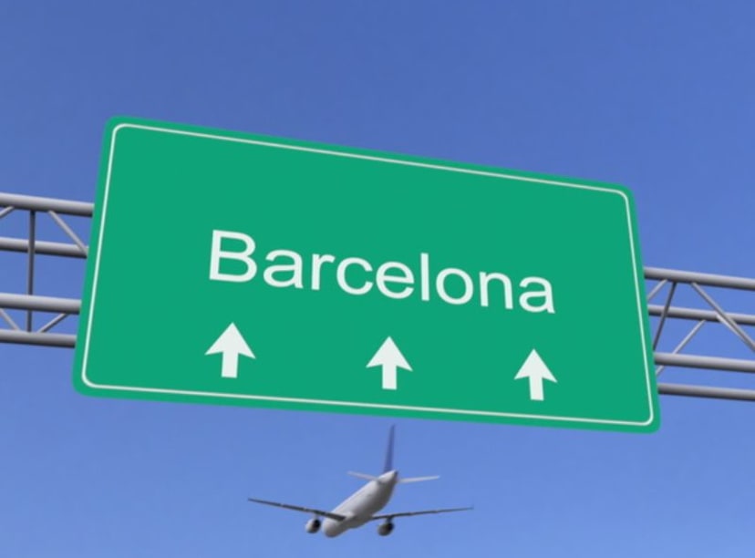 Green overhead traffic sign for Barcelona against blue sky, with aeroplane in background