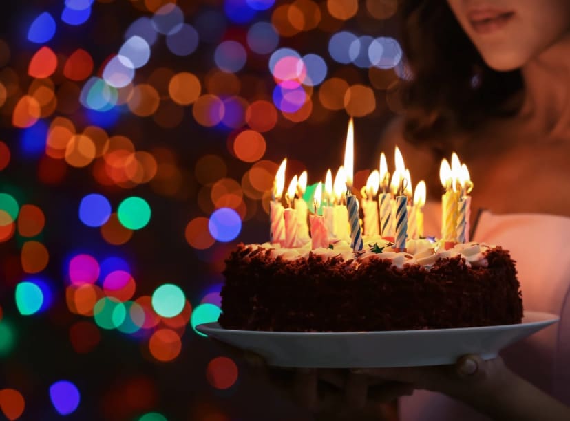 A birthday cake with lit candles brought in on a white plate