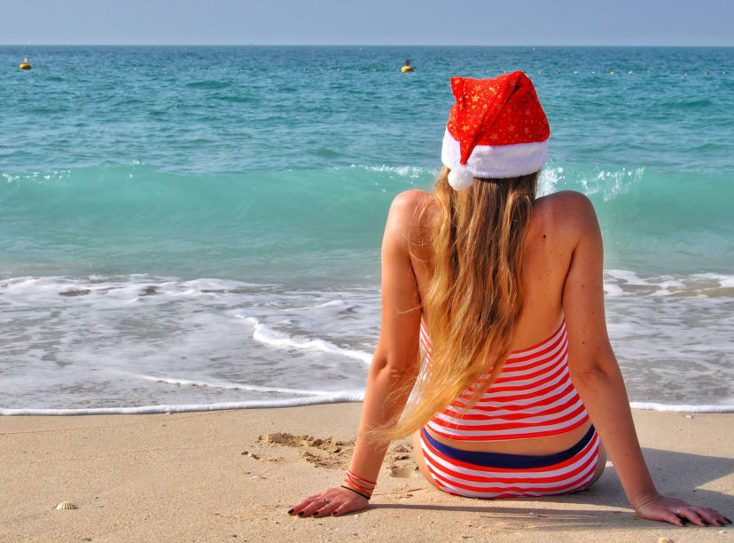 A woman on a beach facing the sea in a Santa hat