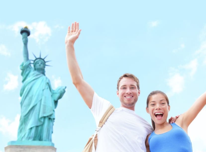 Man and woman wave excitedly echoing the raised arm of the Statue of Liberty in background