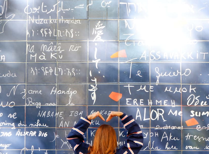 Woman making a heart shape with her arms in front of Montmartre's Wall of Love