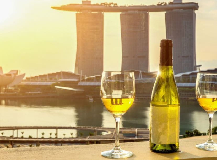 Bottle of wine and two glasses against silhouette backdrop of Marina Bay Sands hotel at sunset