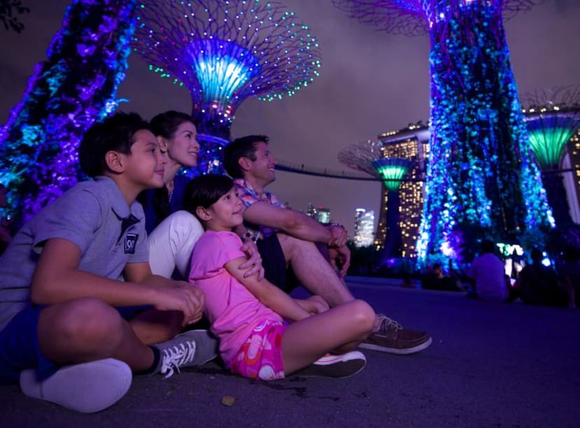 Family sitting on the ground staring up at the blue lit Supertrees of Gardens in the Bay