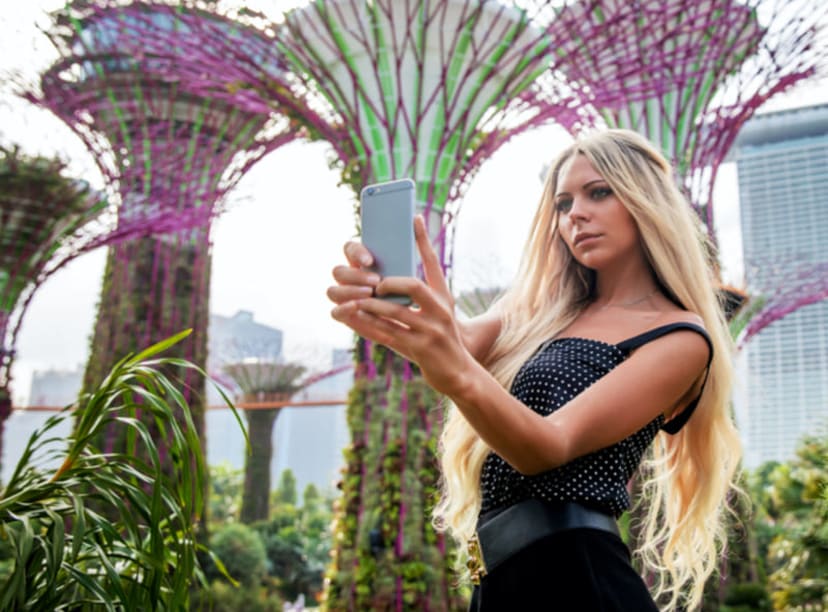 Young woman taking a selfie in front of the super tree structures at the Gardens by the Bay, Singapore
