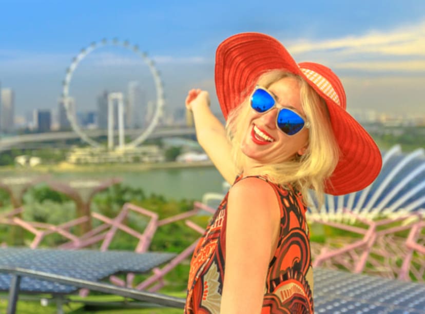 Woman in a red hat smiling and pointing towards the distant Singapore Flyer