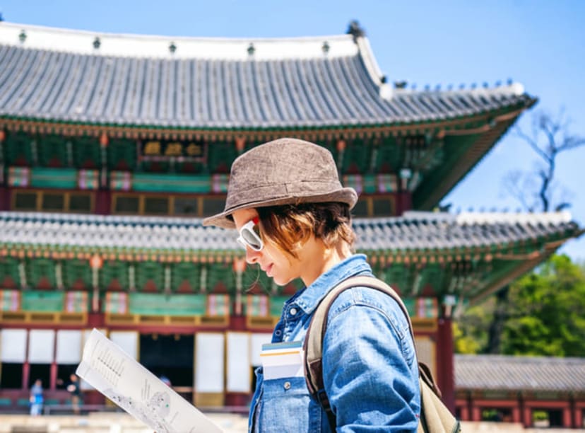 Woman studying a map in front of a pagoda-style building in Seoul.