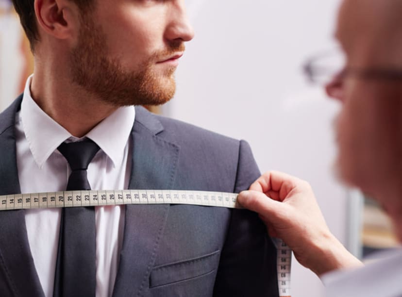 Smartly dressed man having chest measurements taken in a tailor's shop.