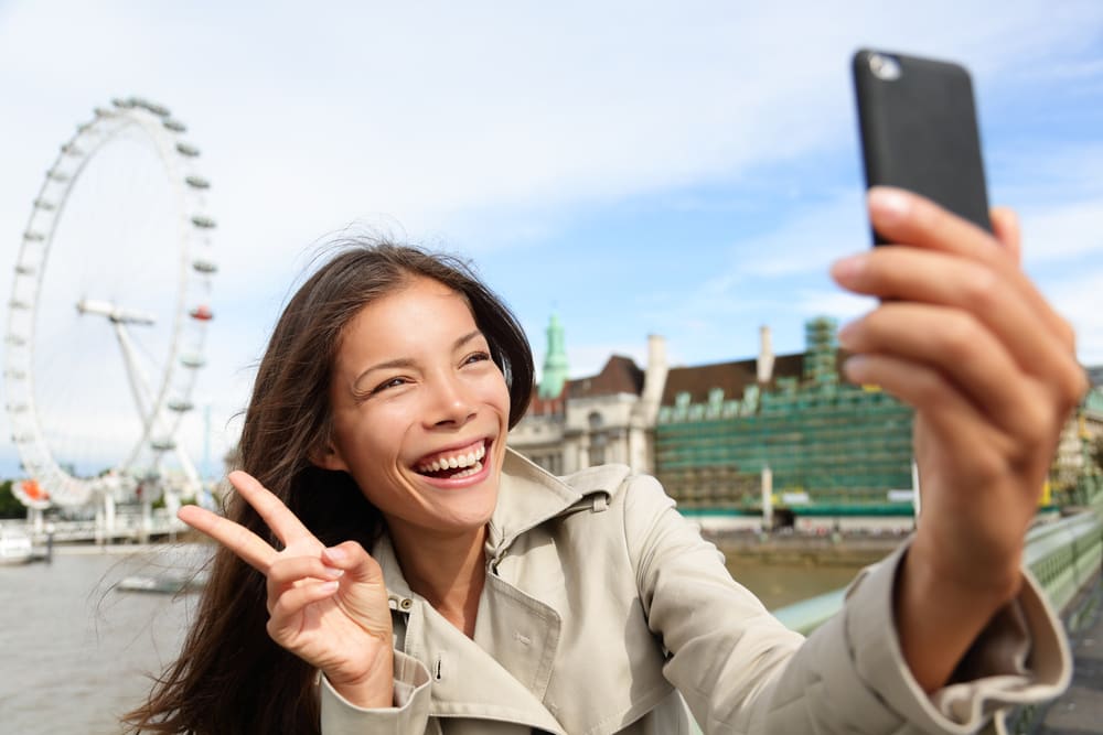 Chica sonriente se hace una foto a sí misma con el London Eye de fondo, Londres.