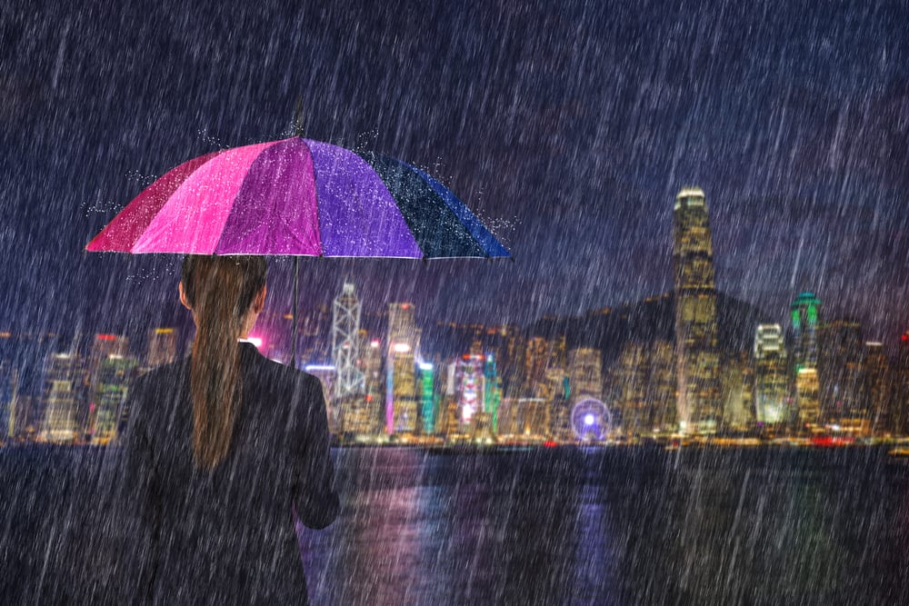 Woman with umbrella gazing at Victoria Harbour during the monsoon