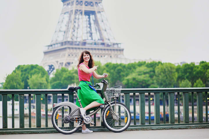 Mujer en bicicleta frente a la Torre Eiffel, París. Medios de transporte en París durante las Olimpiadas.