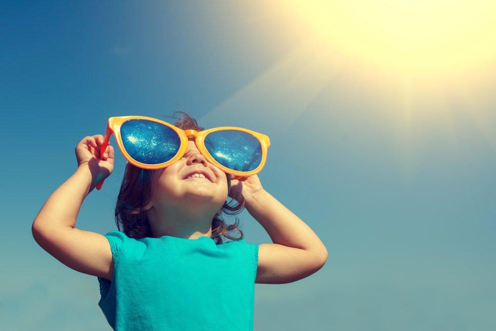 Niño con gafas de sol gigantes mira sonriente al cielo soleado. Junio en San Diego