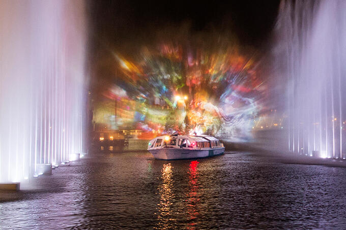 Ein Boot auf den Kanälen von Amsterdam und eine Lichtinstallation im HIntergrund