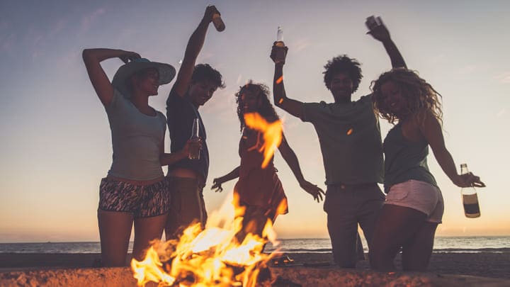 Friends dancing and partying around a beach bonfire