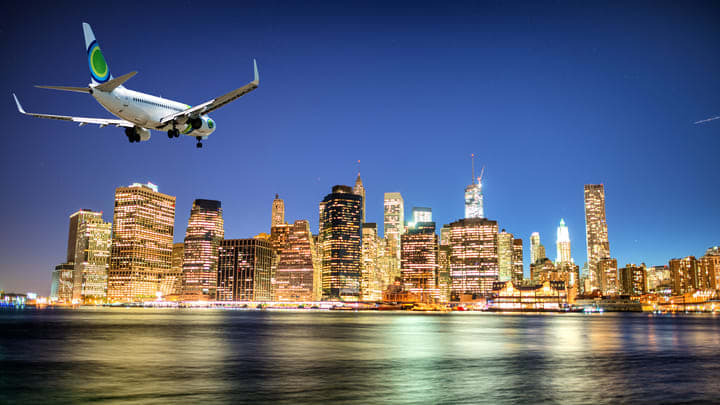 Avión sobrevuela Nueva York de noche. Opciones de transporte desde los aeropuertos de Nueva York.