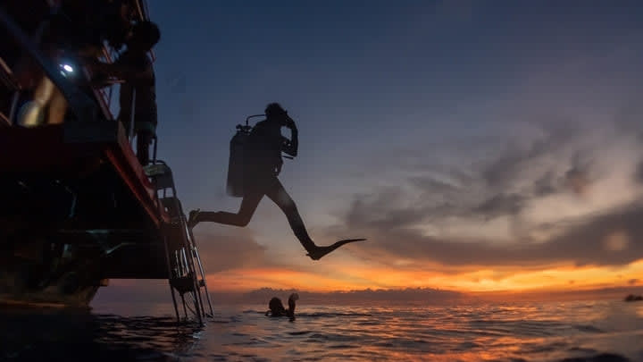 Night diver in full scuba gear jumping from a boat