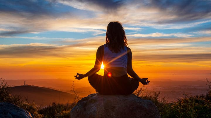 Woman meditating on a mountain at sunset